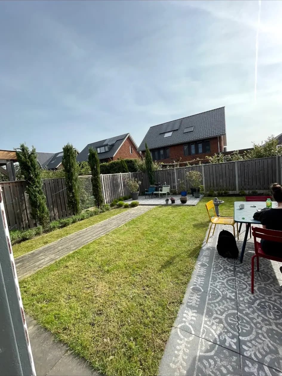 Achtertuin met nieuw gazon, een pad van tegels en een zitgedeelte bij de schutting